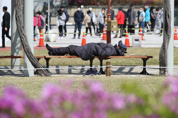 5일 오후 대구 중구 국채보상운동기념공원에 마련된 임시선별검사소 앞에서 시민들이 줄지어 코로나19 진단검사를 기다리는 가운데 노숙인이 공원 벤치에서 누워 낮잠을 청하고 있다. 뉴스1